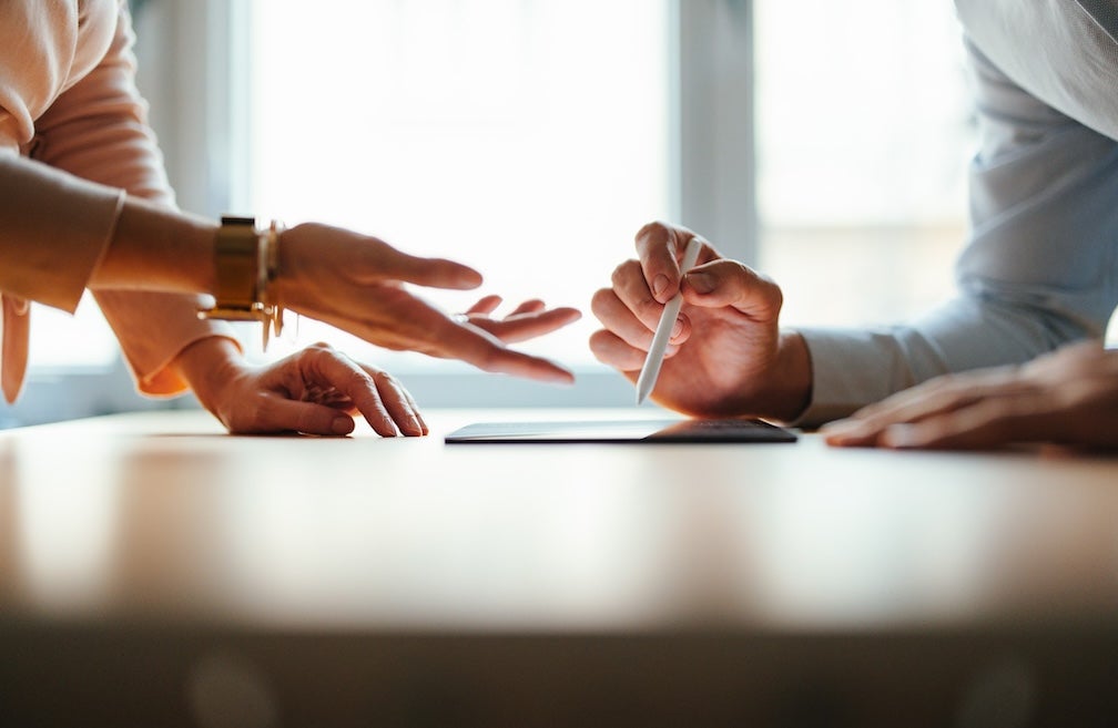 Anonymous team of two colleagues talking and reading business report on a tablet while standing at office desk together.